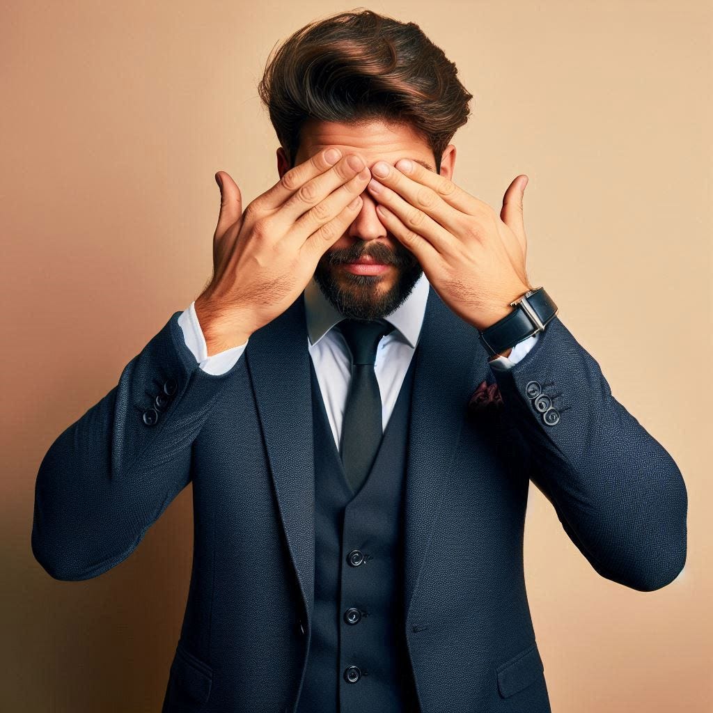 A man with a short beard and a suit with his hands over his eyes
