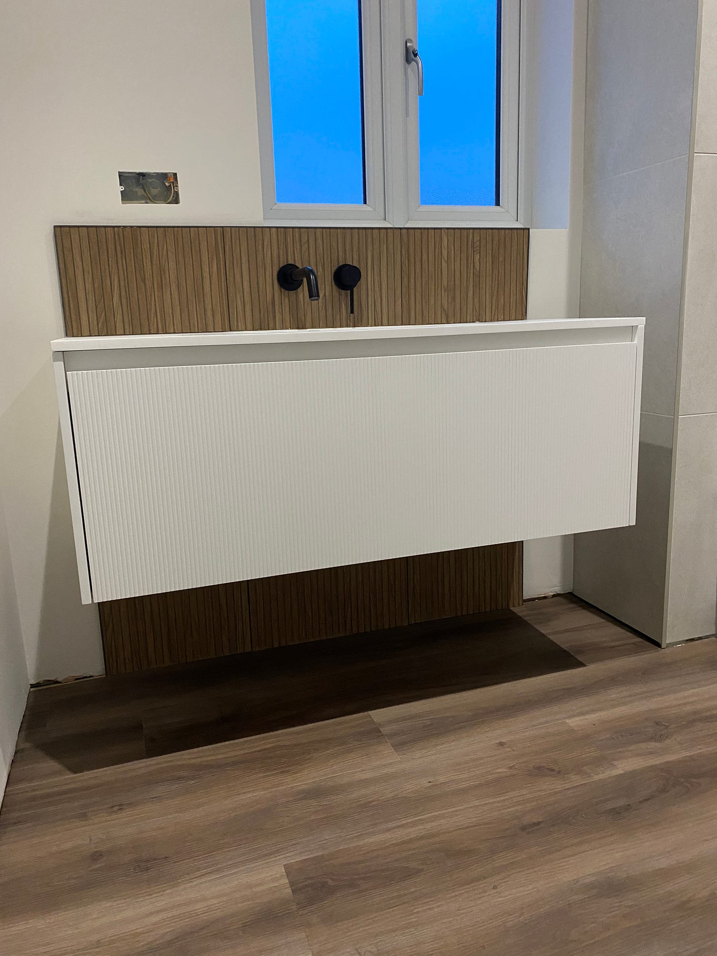 white vanity unit with black tap and brown splash-back