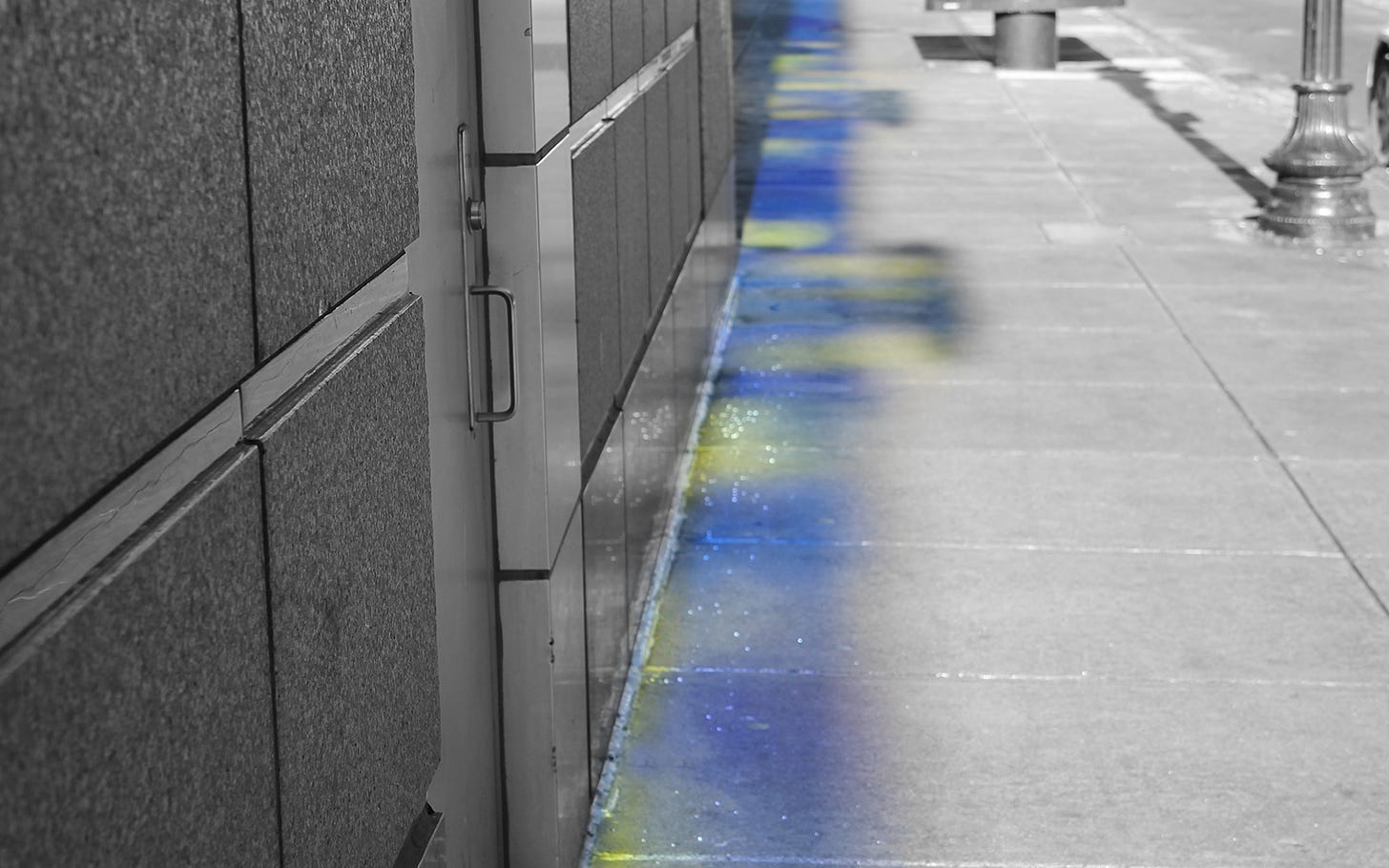 Black and white photo of a city street with a blue and yellow spectrum cast from windows onto the sidewalk.