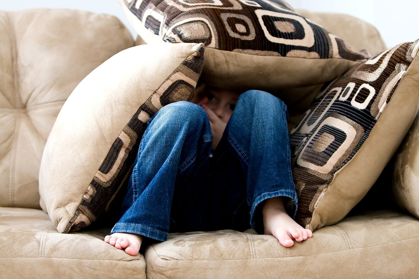 young boy hiding in fear under cushions