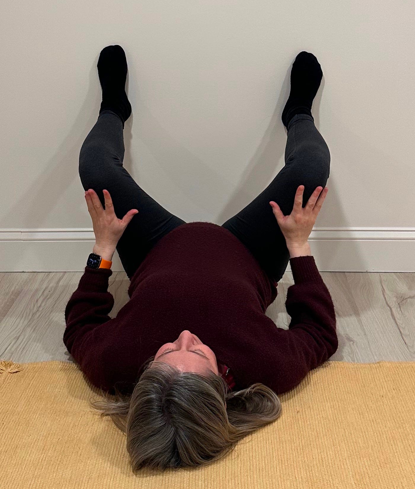 Woman lying on ground with feet on the wall in a squat position