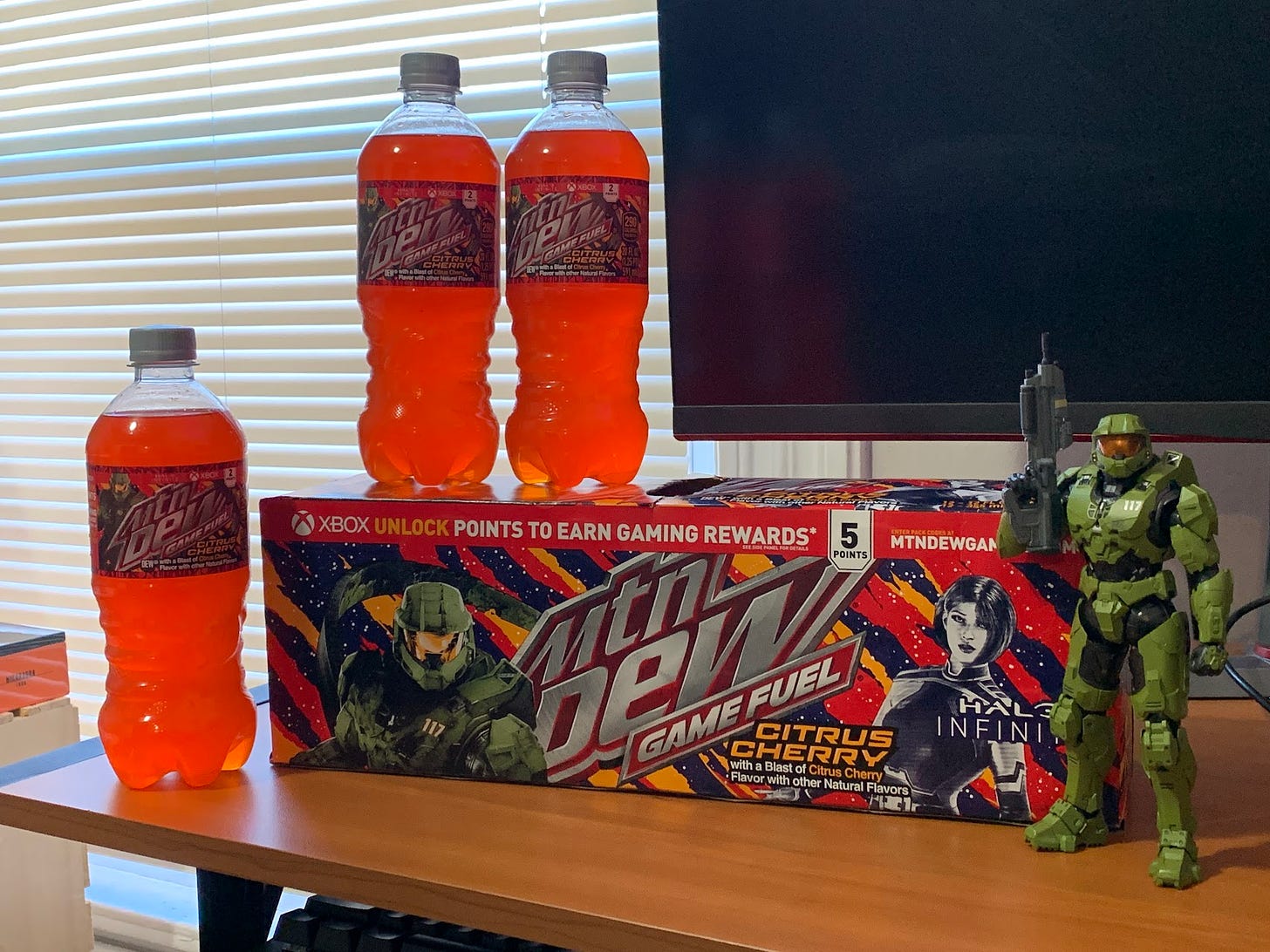 Several bottles and cans of the newly released Citrus Cherry Mountain Dew rest on this writer's desk, as a Master Chief figure stands guard.