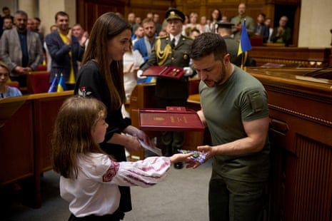 Ukrainian president Volodymyr Zelenskiy gives the daughter of fallen soldier Oleksandr Lukianovych a present while her mother, Anna, receives the order 'Hero of Ukraine' for her fallen husband during a session of the Ukrainian parliament dedicated to the constitution Day.