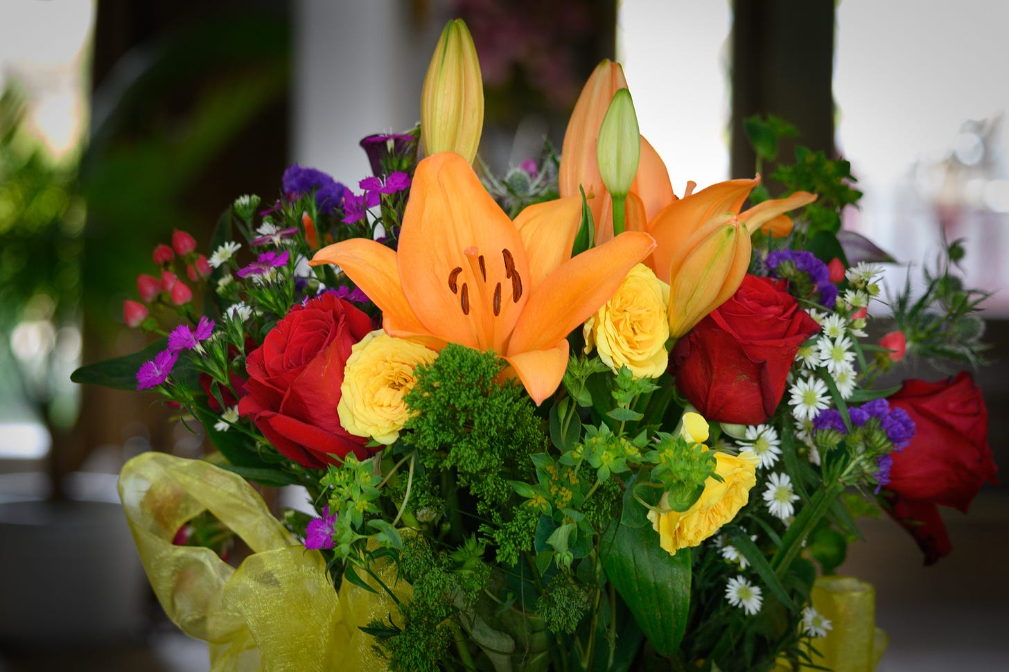 A mixed bouquet of flowers with roses, assorted flowers and greenery, and orange lilies 