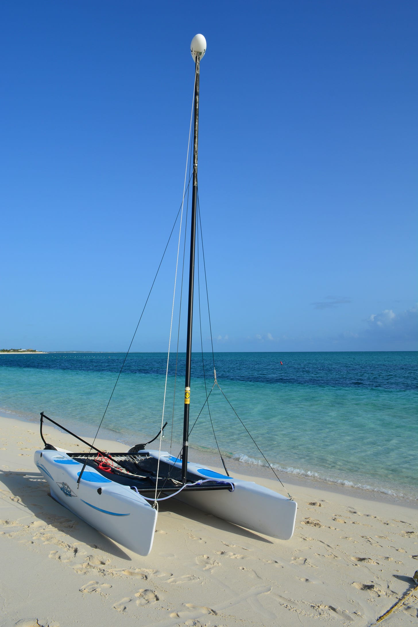 A white-hulled catamaran sits on the sandy beach with the turquise water of the ocean n the background