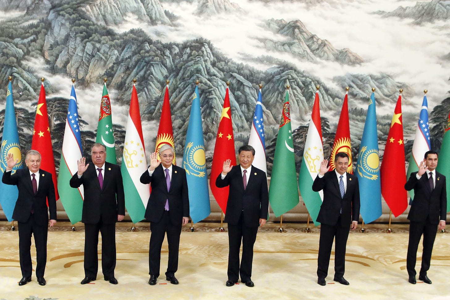 Several men in suits waving in front of flags

Description automatically generated