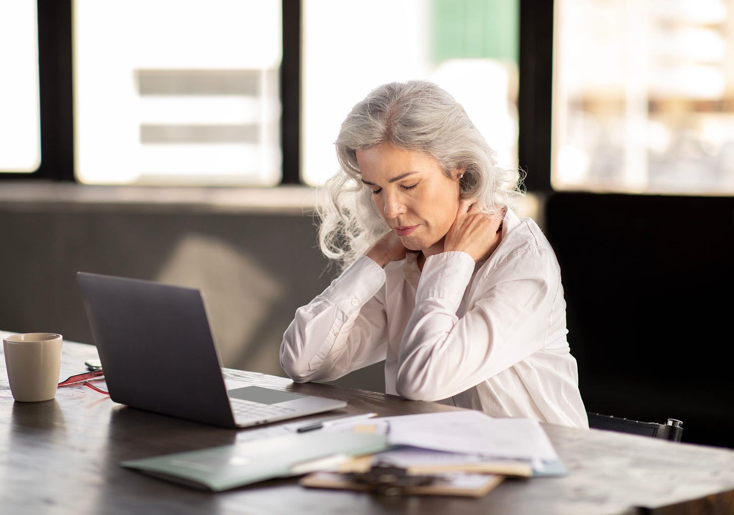 Older lady sat in an office touching her achy neck