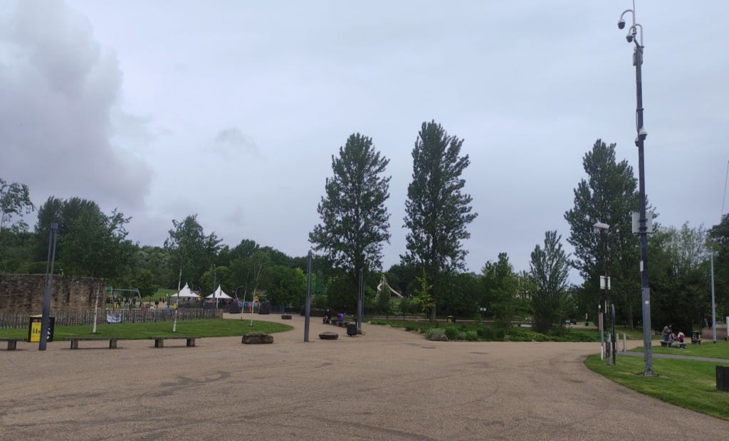 Wide paths outside the visitor centre and playgrounds with a few tall trees.