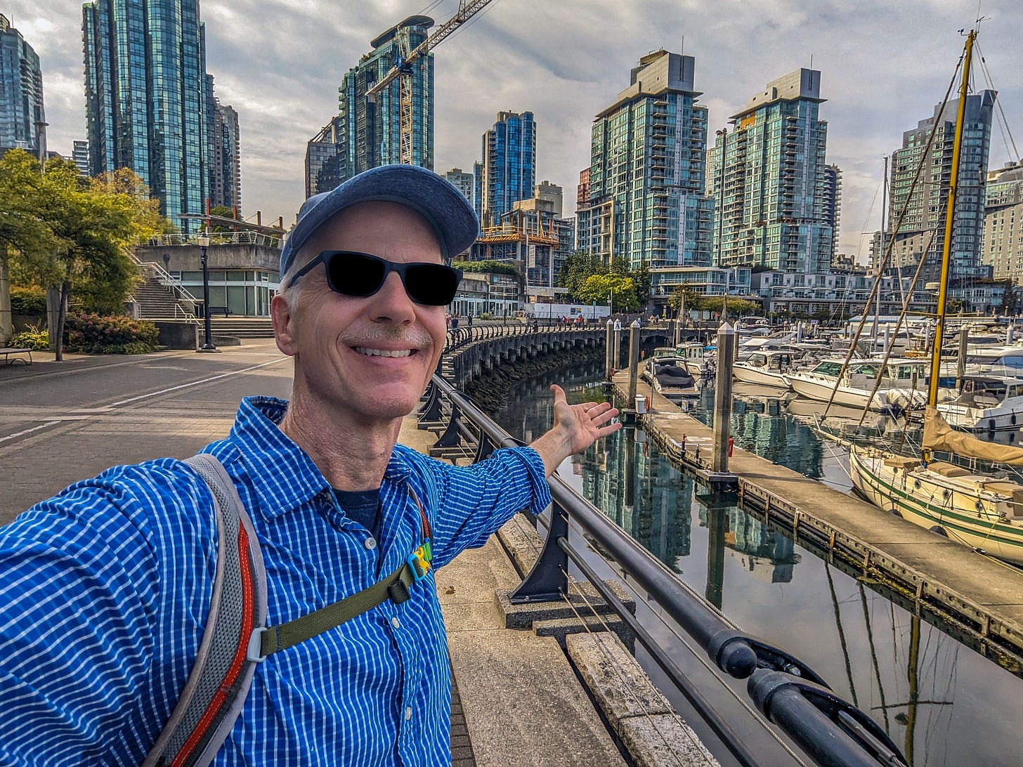 Michael standing on the waterfront gesturing at boats on the water and condos in the background. 
