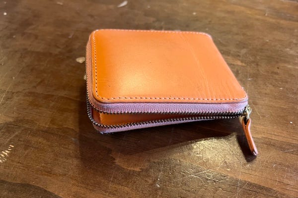 A photo of an unzipped, square orange leather wallet.
