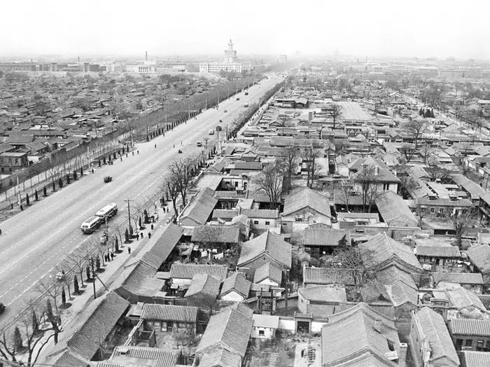 A sinistra un'ampia strada; a destra un vecchio quartiere di Pechino. Foto in bianco e nero