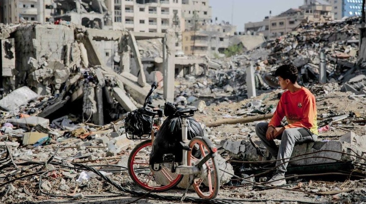 A Palestinian youth sits next to his bike amid the rubble of destroyed buildings in Gaza City 