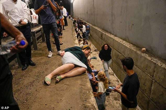 People take cover on the side of a road as a siren sounds a warning of incoming missiles on Oct 1