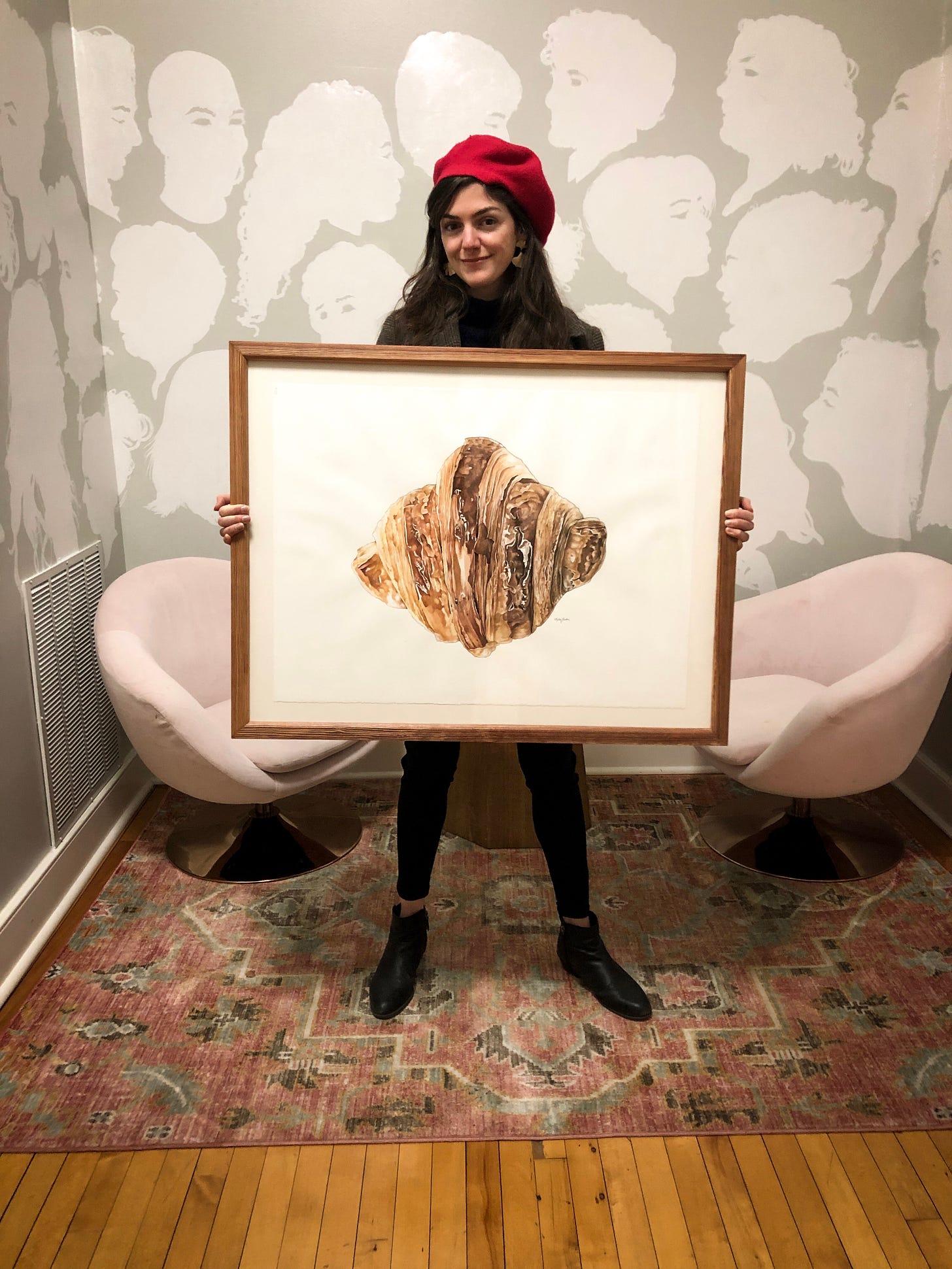 Photo of Molly standing holding the framed watercolor painting of the croissant in front of her