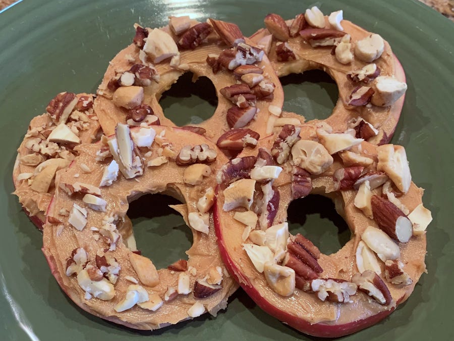 A plate of apple rings covered in peanut butter and topped with choppped nuts