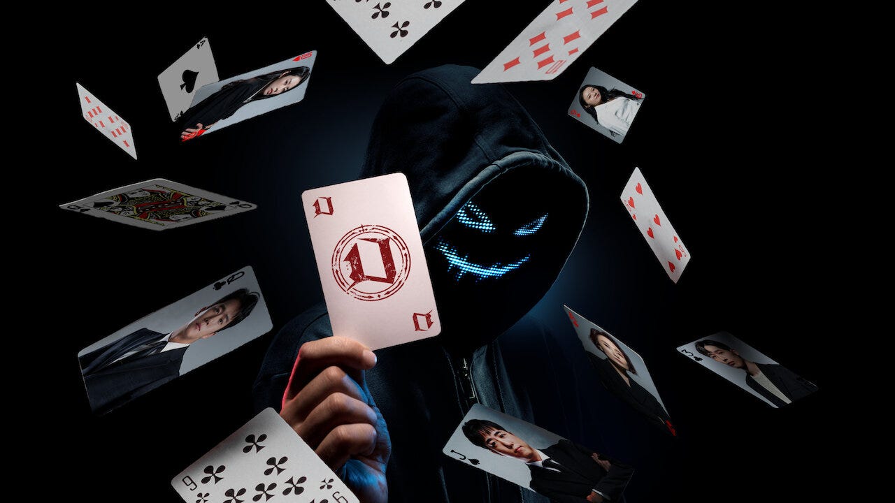 A masked and hooded man surrounded by playing cards with the faces of contestants on them holds up a card with the Devil's Plan logo on it.