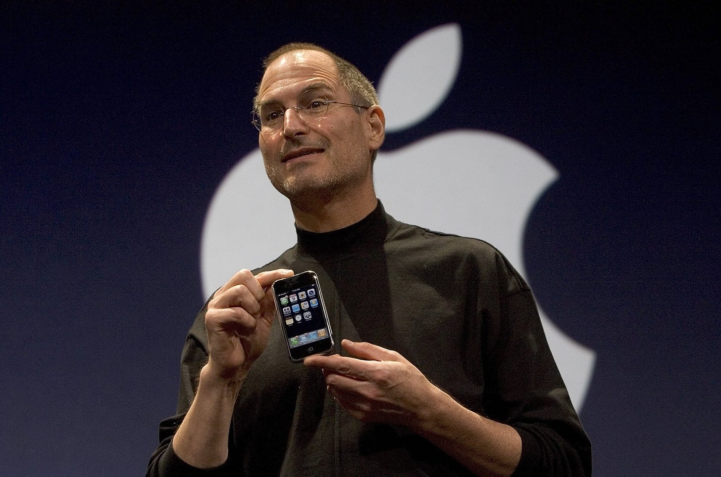 Steve Jobs tiene l'iPhone davanti al logo Apple.