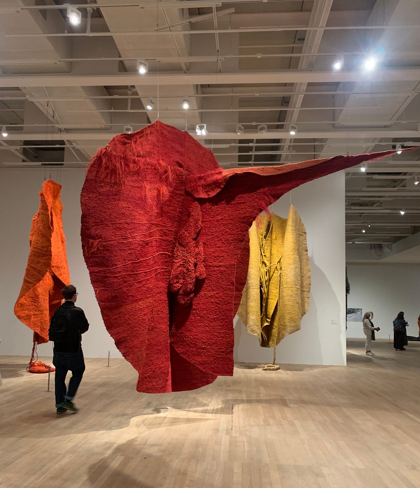 Three large fabric sculptures, one orange one red and one yellow suspended from the ceiling in an art gallery