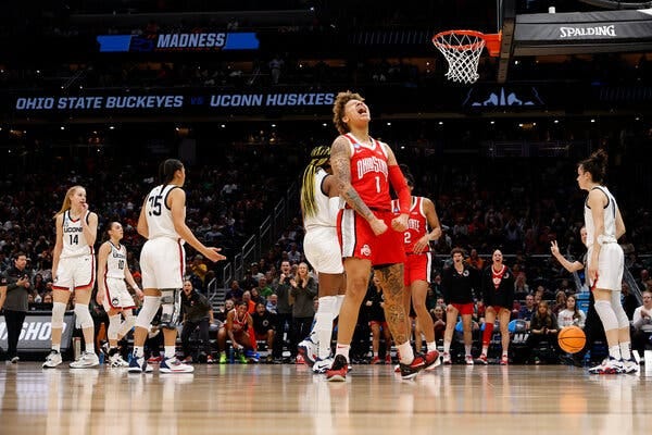 Ohio State’s Rikki Harris, in a red No. 1 jersey, throws her head back yelling while flexing her arms, as UConn players mill about behind her on the court.