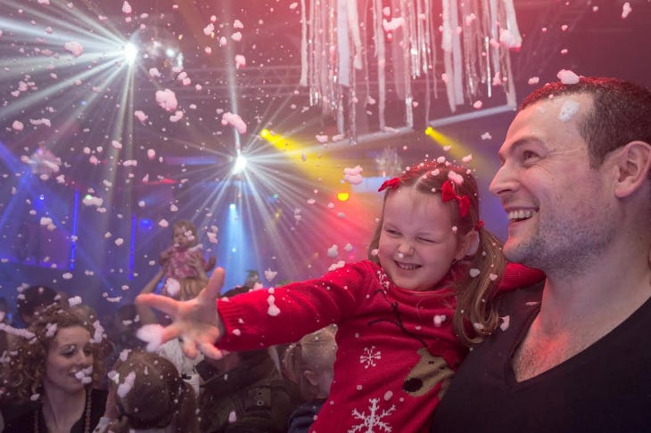 A man carrying a little girl on a dance floor, as fake snow or foam falls