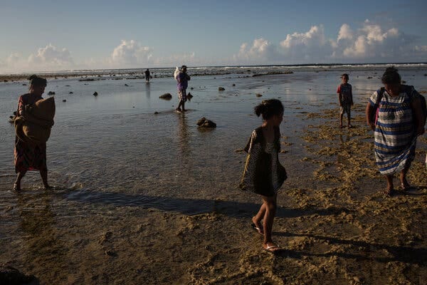 People walk between islands during a rising tide. The sand is covered by only a few inches of water. 
