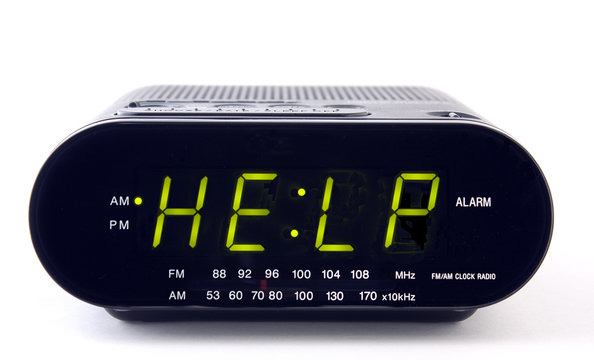 A digital alarm clock with bright green text on the screen reading: "HELP".