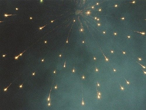 This may contain: fireworks are lit up in the sky with green and yellow lights on it's side