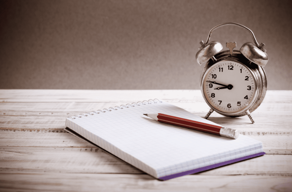vintage-alarm-clock-placed-on-wood-table-next-to-pad-and-pencil-tracking-peak-performance