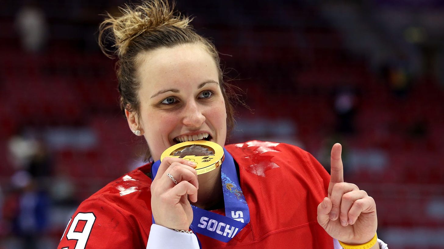 Marie-Philip Poulin biting a gold medal and making the number one sign with her hand.