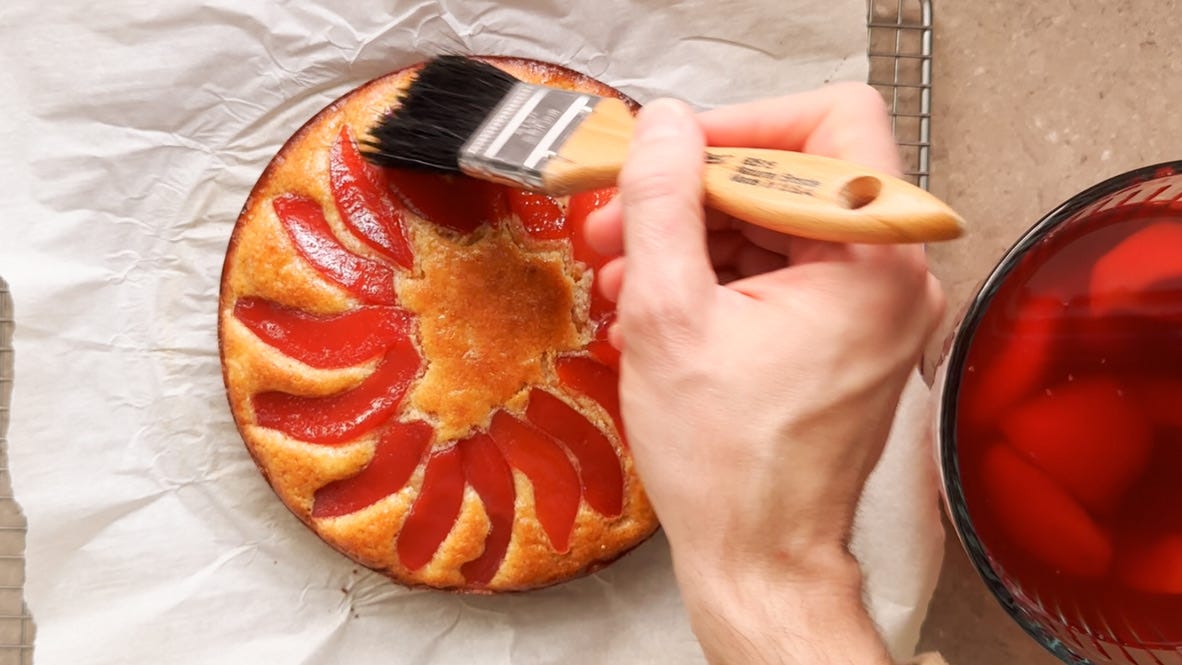 A photo of a hand brushing syrup onto a baked quince cake.