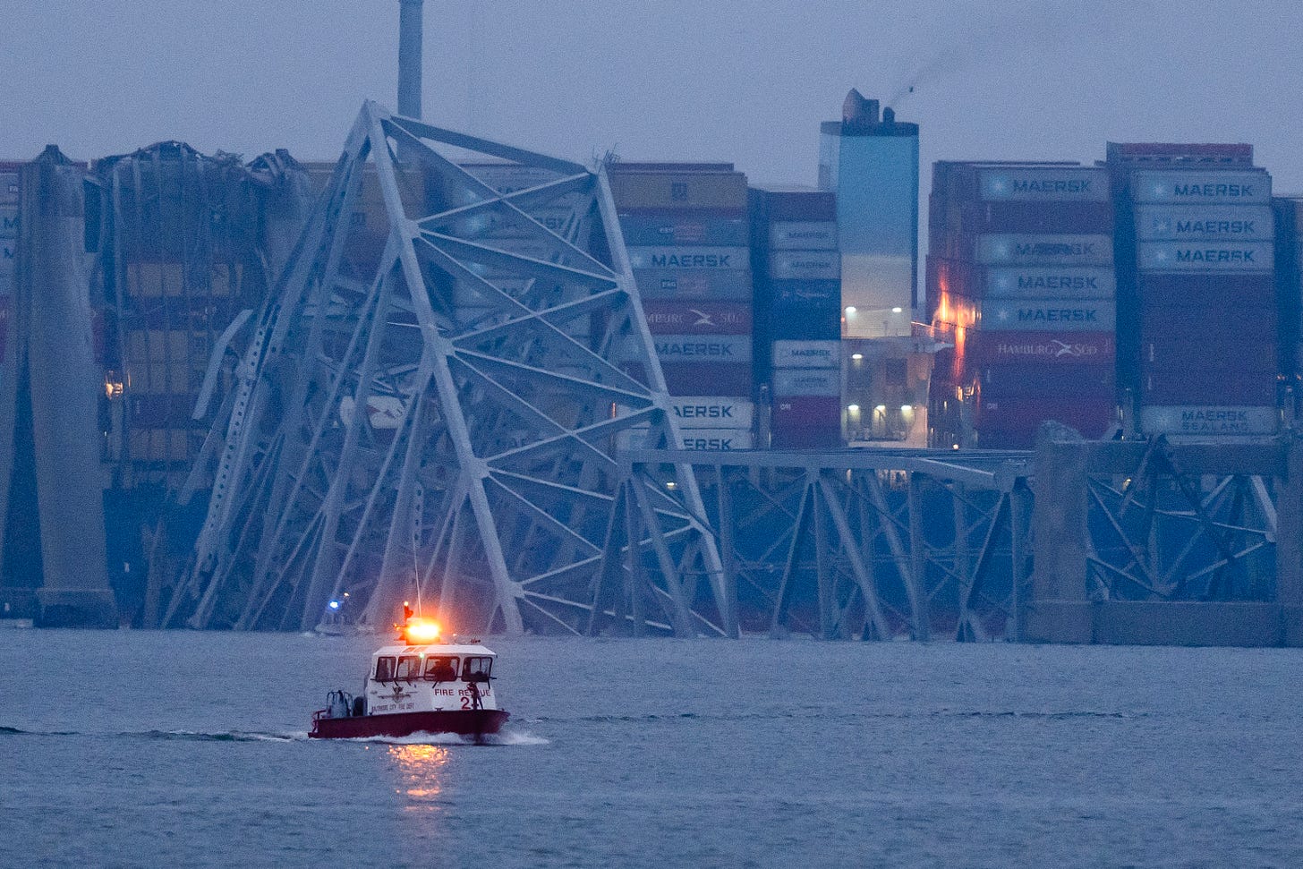 A container ship rests against wreckage of the Francis Scott Key Bridge near sunrise.