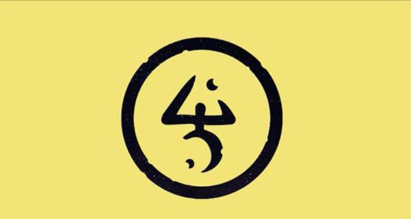 uma imagem de fundo amarelo com um símbolo sobreposto em preto, envolto por um círculo. O formato do símbolo envolve formas geométricas incompletas, aparentemente duas luas minguantes abaixo e um triângulo para cima, conectados por um único traço preto.
