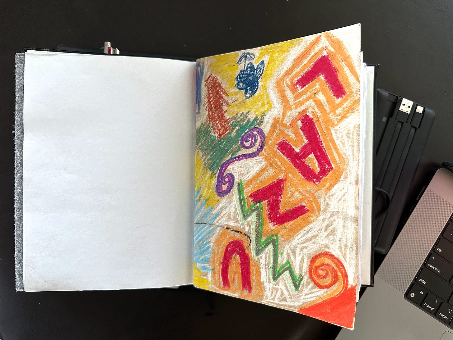 An open notebook on a dark background, with an adult’s crayon drawing on brown paper on the right hand page.
