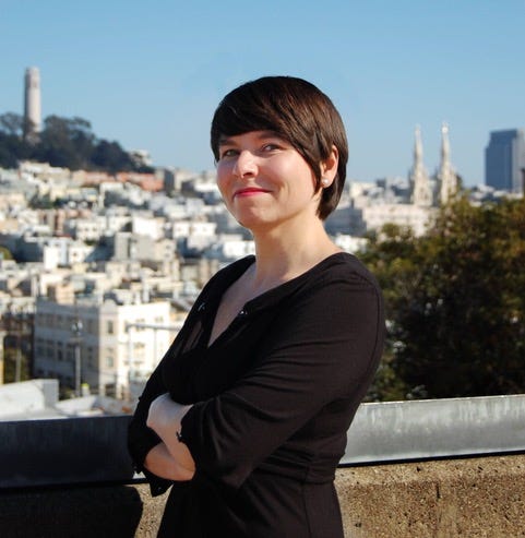 Melody Hernandez smiling and looking stylish in a black outfit, with Coit Tower and San Francisco in the background