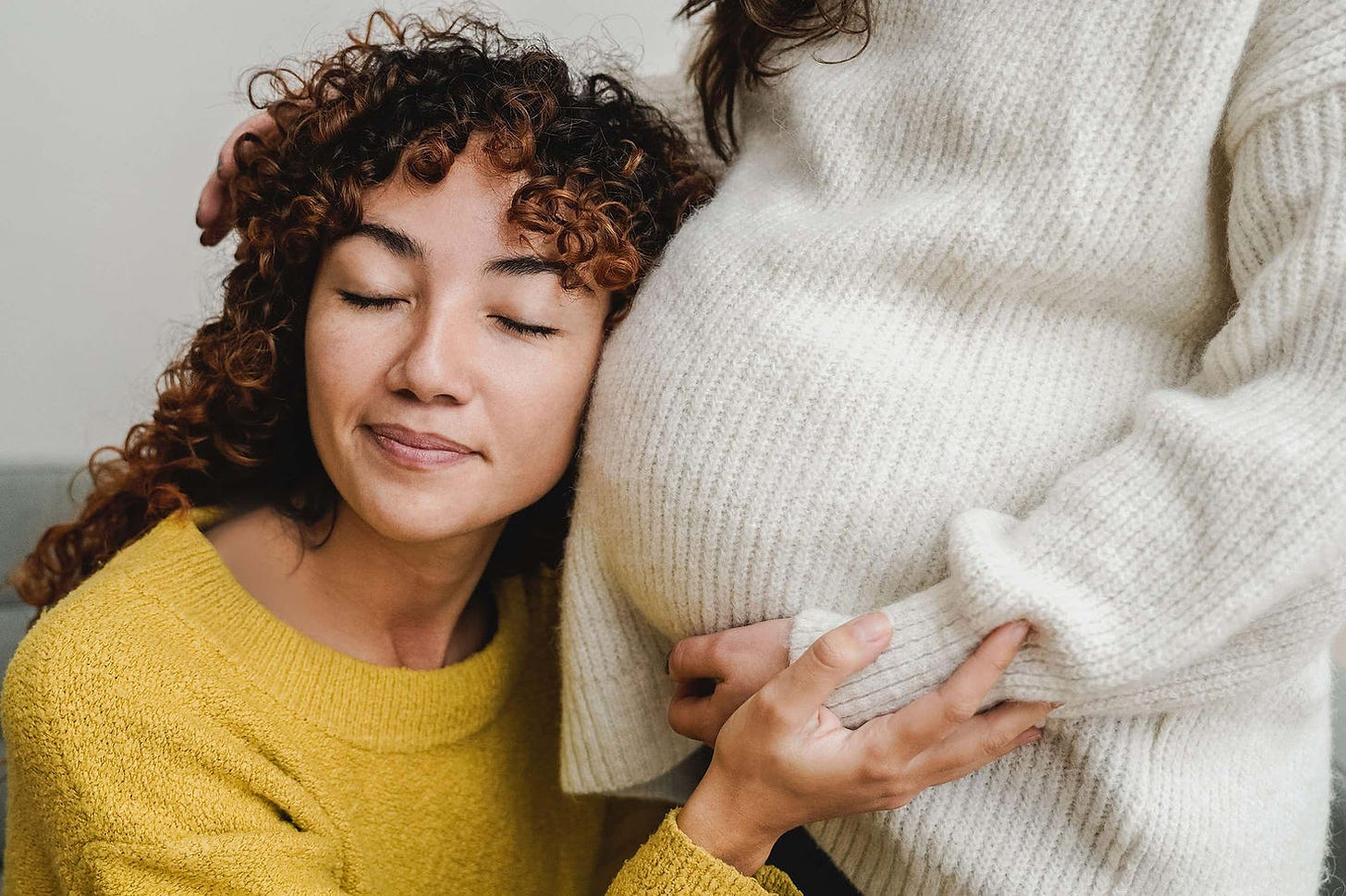 Gay female couple having tender moment listening her pregnant wife baby belly