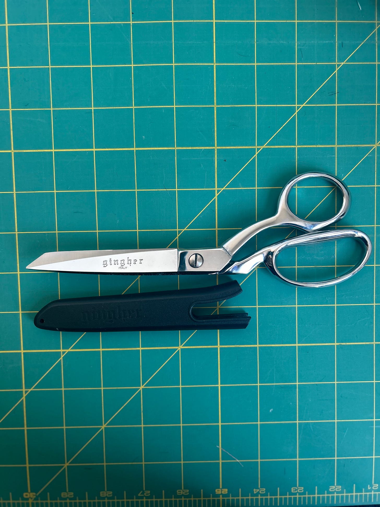 A pair of Gingher fabric scissors on a green background
