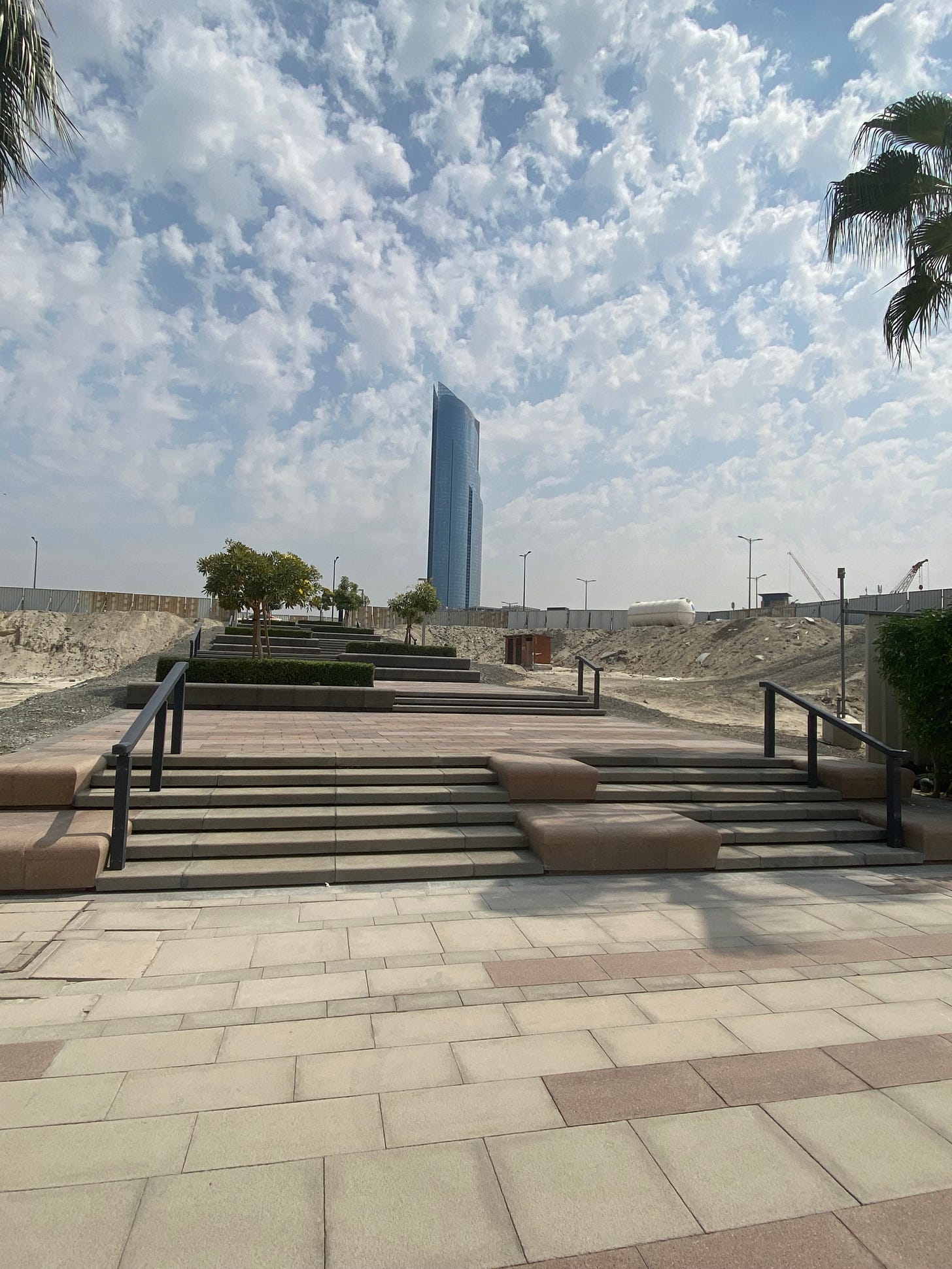 Photo of the last set of stairs in the Sound Walk with a backdrop of a glass tower and passing clouds above