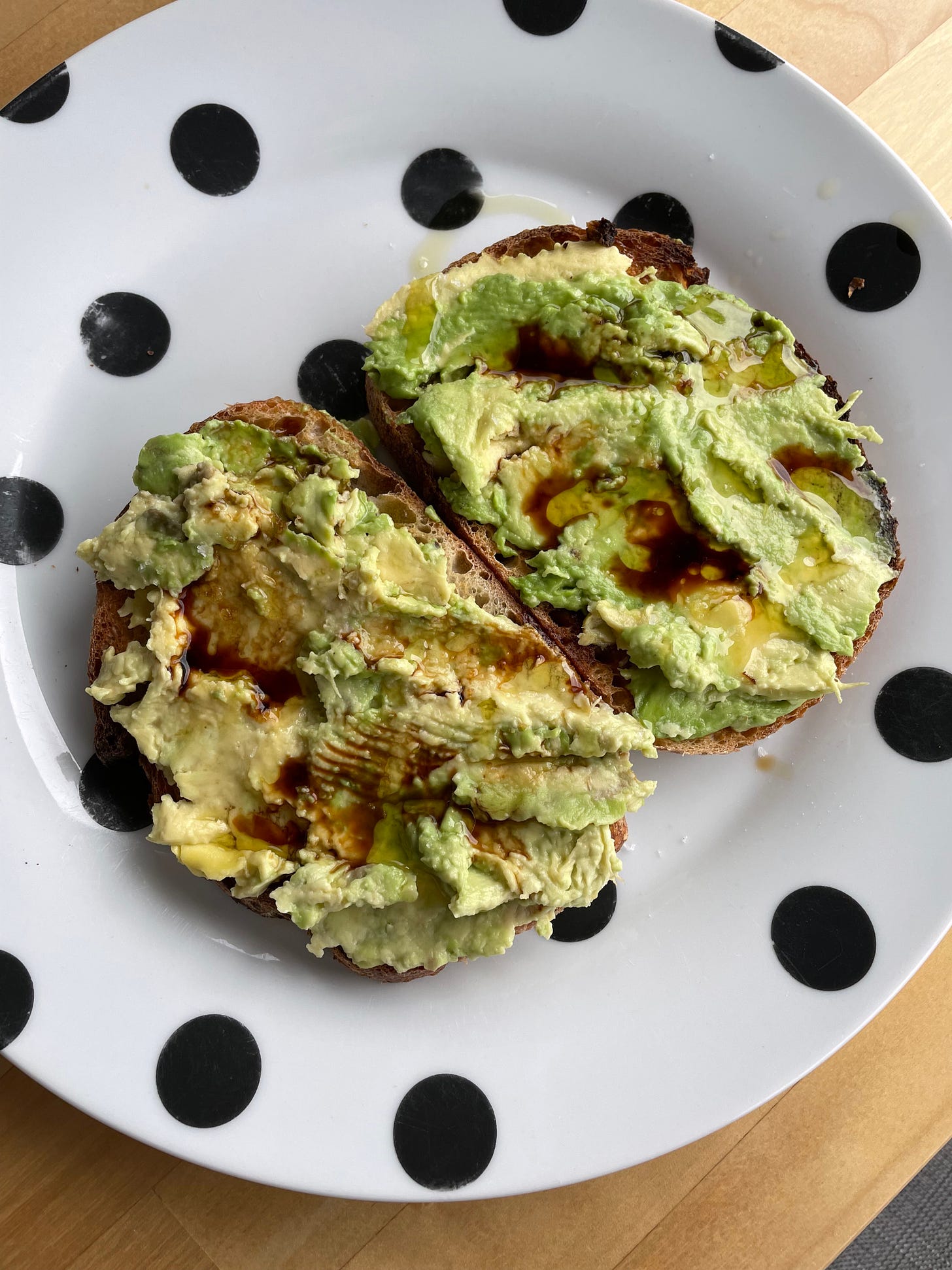 Avocado toast topped with balsamic vinegar and olive oil on a spotted plate.