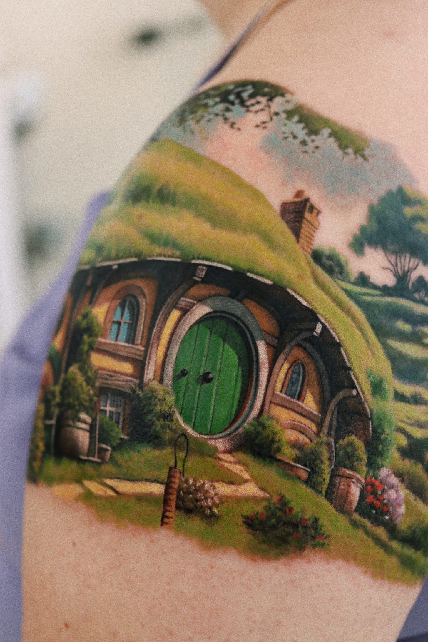 A tattoo depicting a charming hobbit house on a woman's arm, highlighting its unique architecture and vibrant colors.