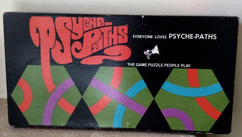 May include: Psyche-Paths game box cover with red, green, blue, and purple geometric shapes on a black background. The text reads 'Psyche-Paths', 'Everyone loves Psyche-Paths', and 'The game puzzle people play'.