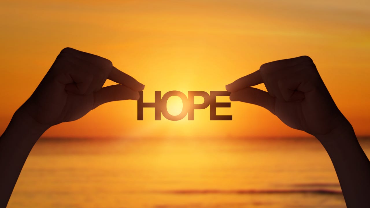A person holding the word "Hope" in front of the sun.
