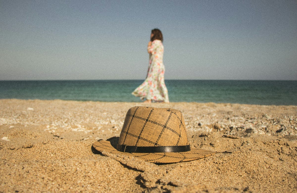 Person walking on the beach and a hat in the foreground Person walking on the beach and a hat in the foreground