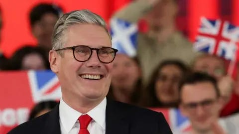 Reuters A smiling Sir Keir Starmer surrounded by cheering supporters, waving union jacks
