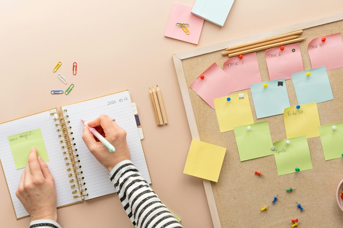 corkboard with post it notes and person writing in notebook