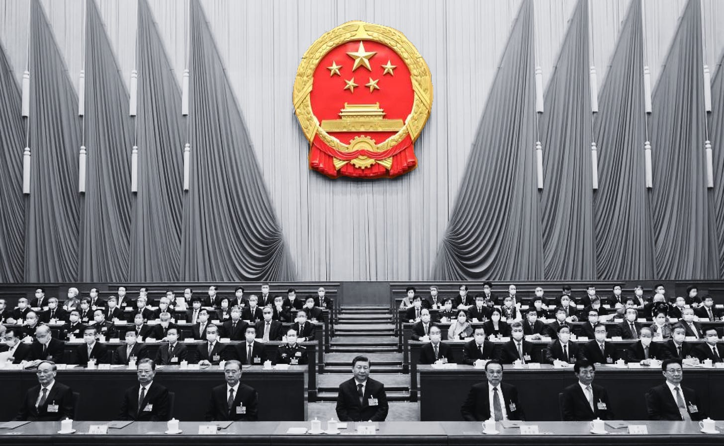 Xi Jinping sitting at the center of the National People's Congress in 2022 in black and white with the National Congress seal in bright red and gold over the meeting