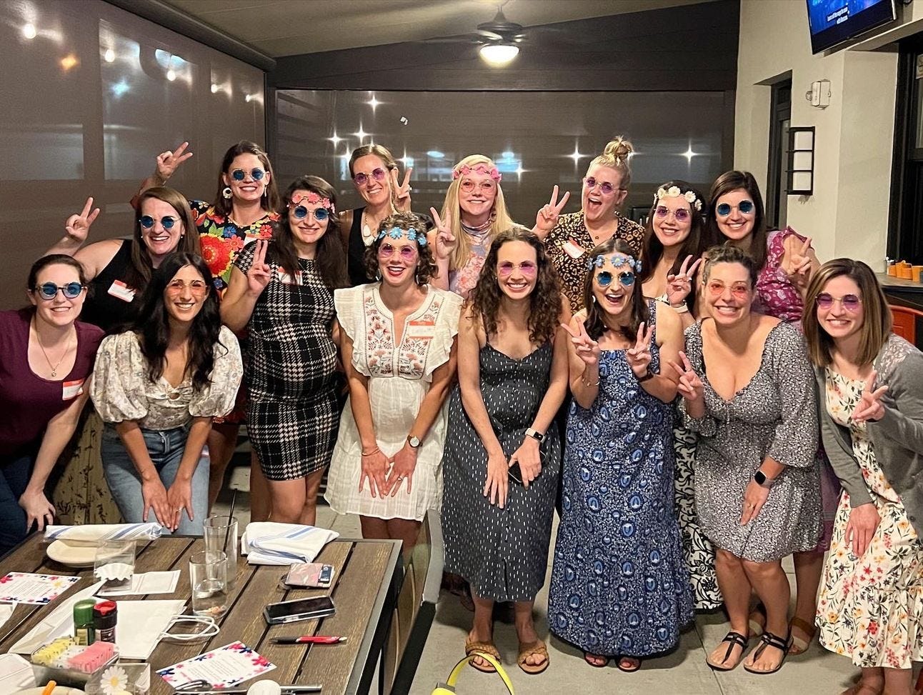A group of women gathering together in a picture wearing 70s attire and showing the peace sign with their hands. A group of women gathering together in a picture wearing 70s attire and showing the peace sign with their hands.