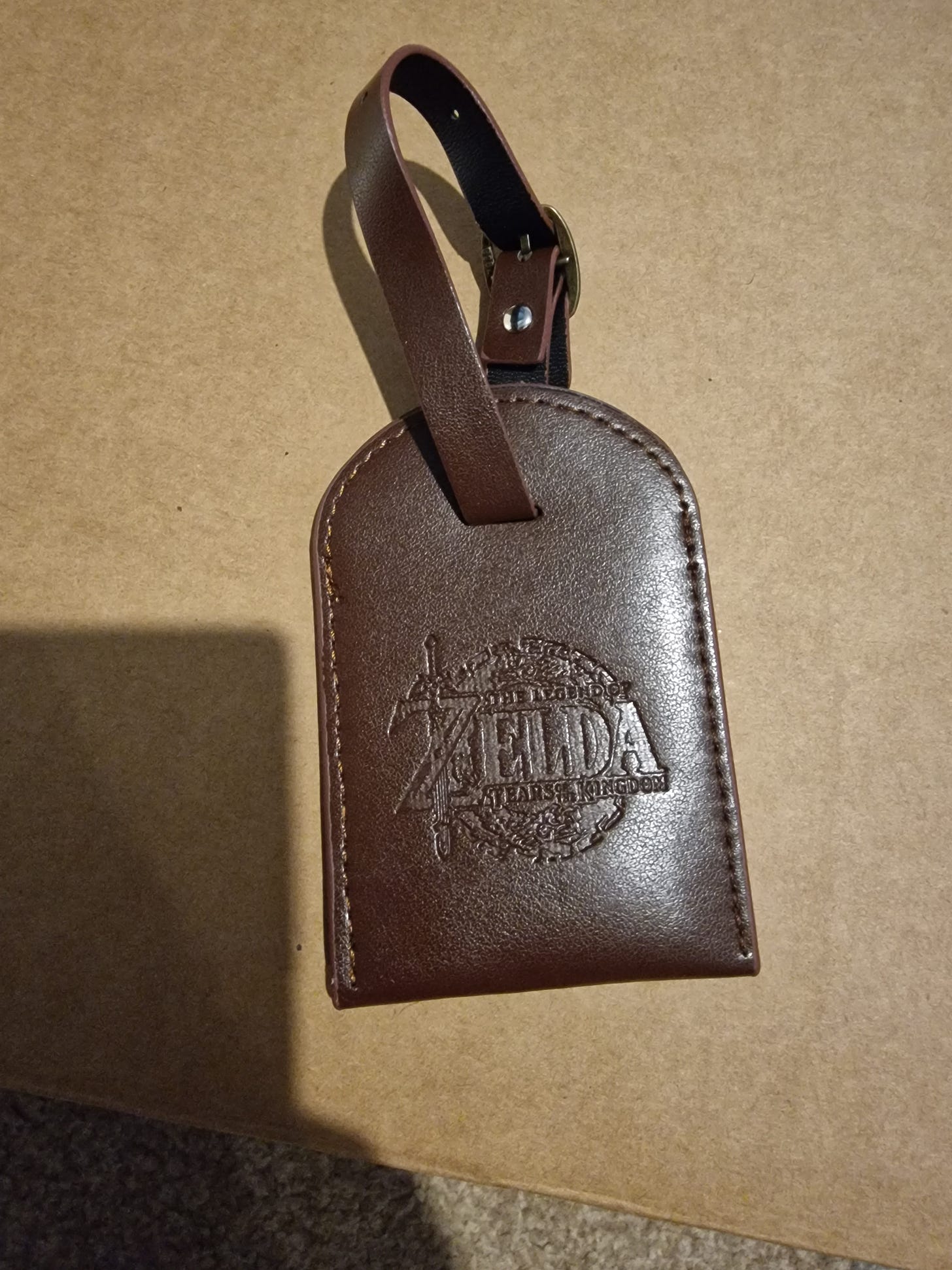 A dark brown leather look luggage tag with the logo embossed on it