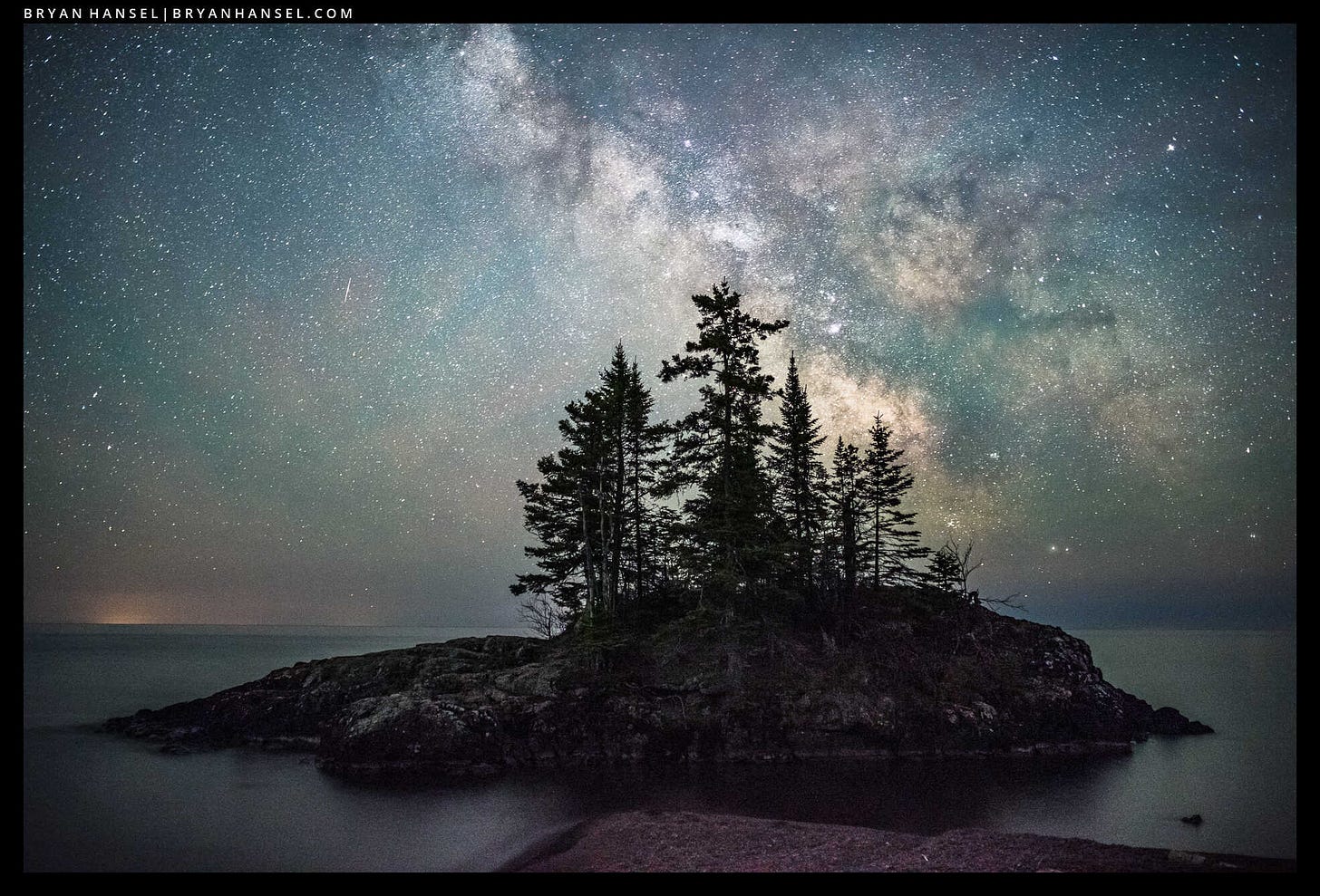 The Milky Way over Lake Superior. A small island with quirky fir and spruce trees is in front of the Milky Way.