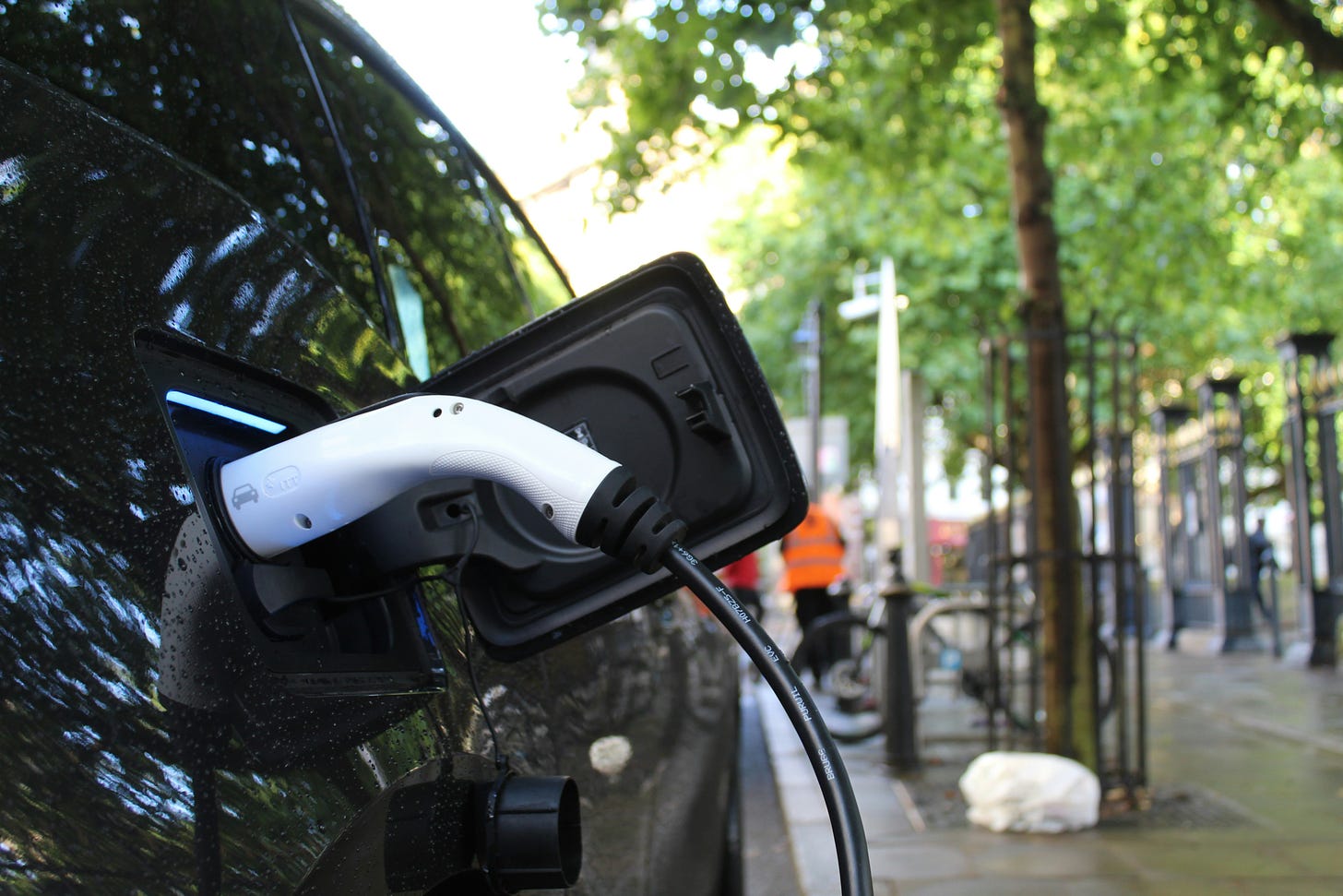 An electric vehicle charger plugs into a black EV on the side of the road.