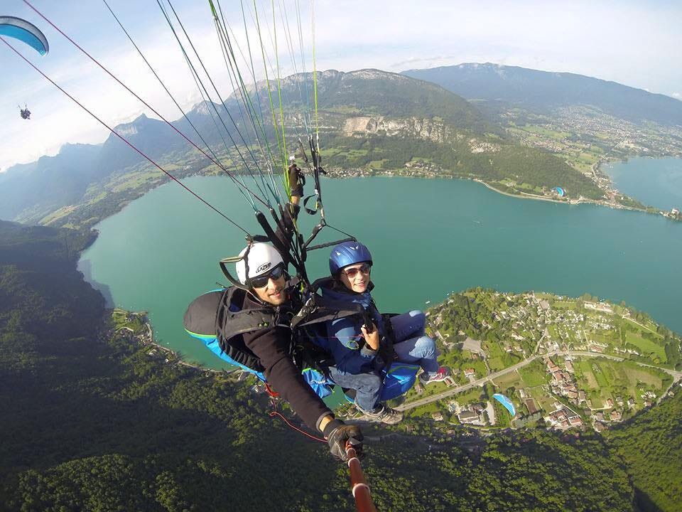 A person paragliding over Lake Annecy, France, with a stunning aerial view of the turquoise lake, surrounding mountains, and the landscape below, captured on a clear day.